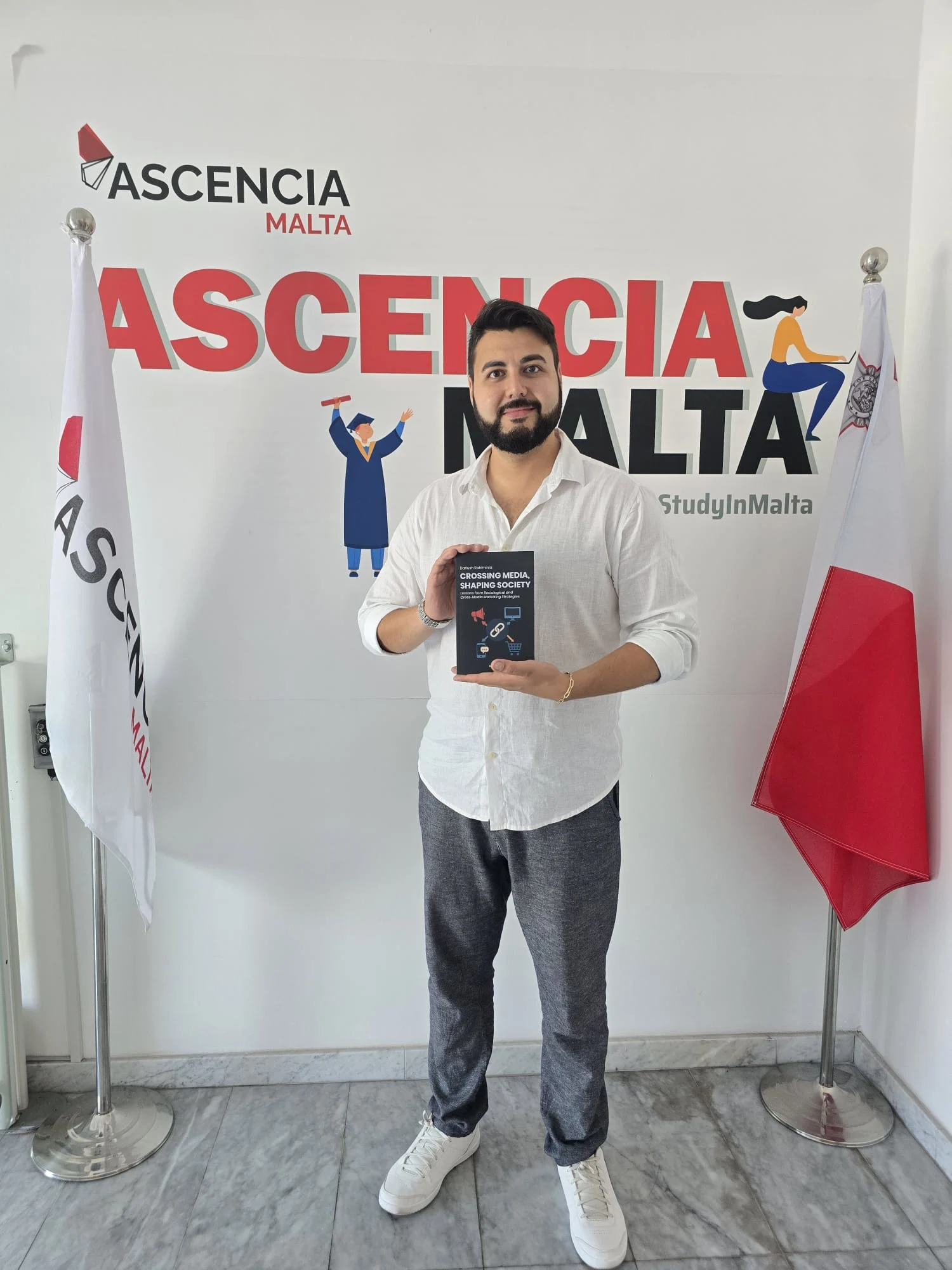 Ascencia Malta Editor-in-Chief Dariush Rahiminia holding his published book at Ascencia Malta campus, showcasing academic publishing success